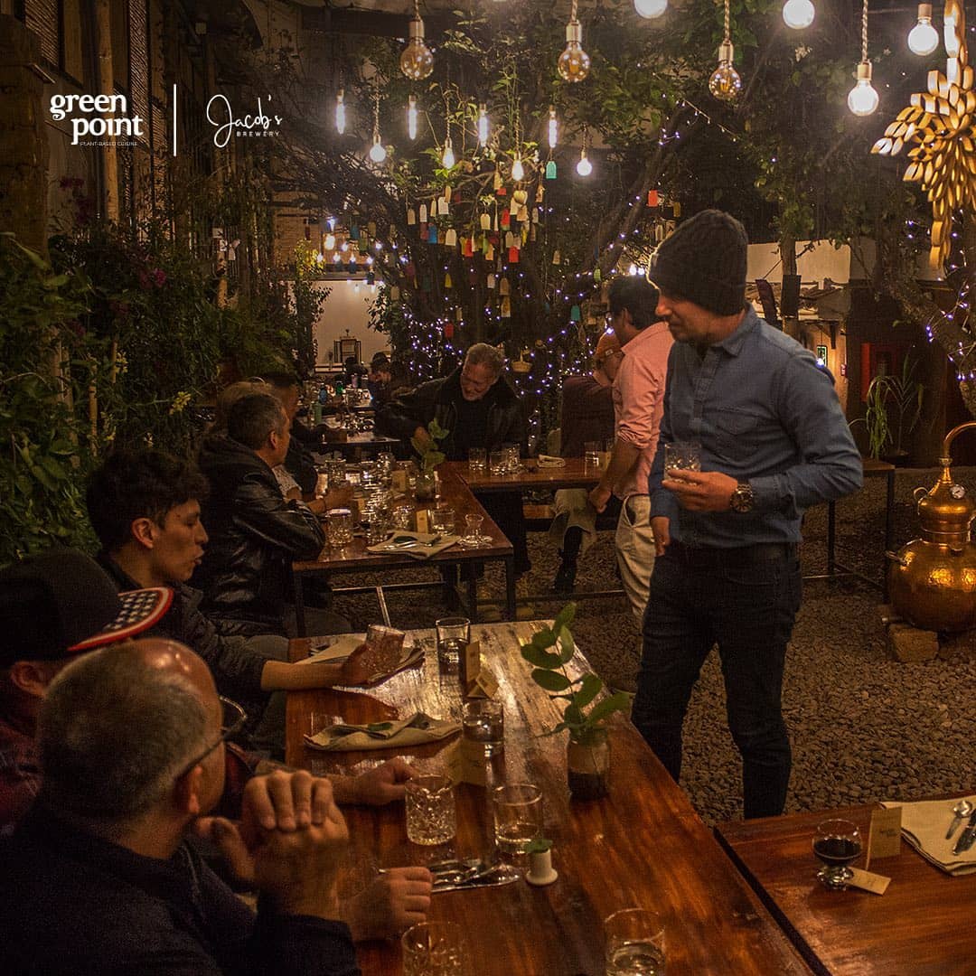 Warm and cozy evening atmosphere at Green Point Jacob's restaurant in Cusco, with patrons dining under a canopy of decorative lights and hanging tags - The Cusco Guide