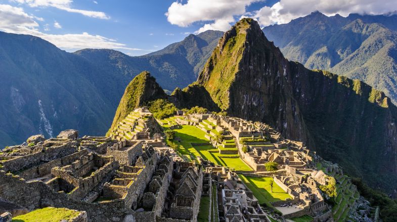 Panoramic view of the historic sanctuary of Machu Picchu, nestled amidst lush green mountains, under a clear blue sky in Cusco - The Cusco Guide